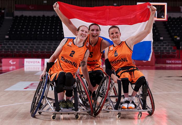 Three female Dutch wheelchair basketball players smile with Dutch flag