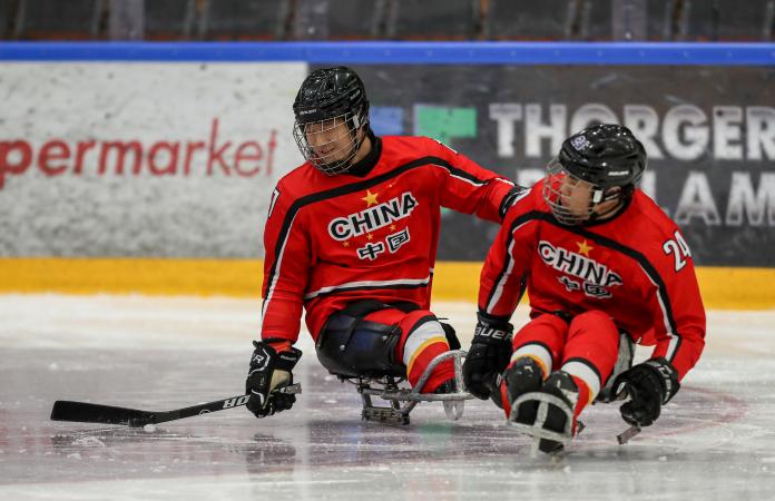 Chinese Para ice hockey player skating on a sled while controlling the puck with his right stick
