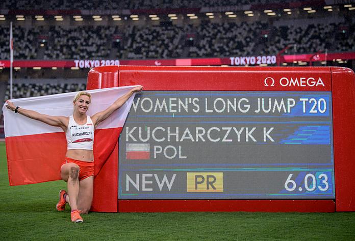 Gold medallist Karolina Kucharczyk of Poland poses next to the scoreboard showing her new Paralympic Record of 6.03 metres. 