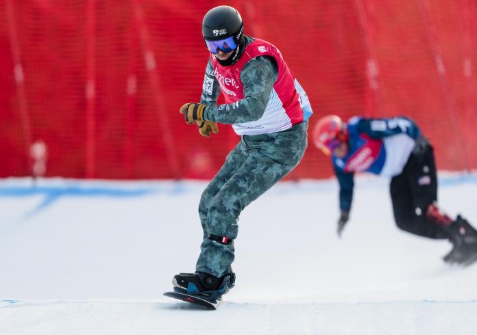 A male snowboarder in a competition with another snowboarder in the background