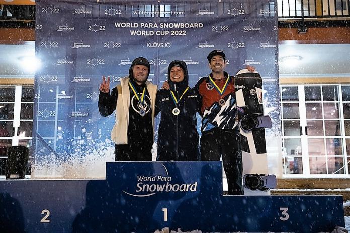 Three men with arms around each other on a snowboard podium