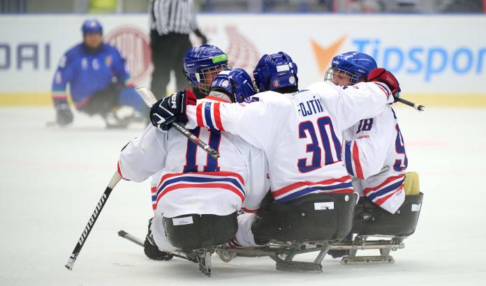 A group of Para ice hockey players on sledges celebrating the victory with a group hug.