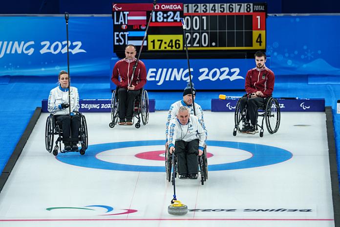 A wheelchair curler from Estonia releases the stone watched by his teammates and opponents