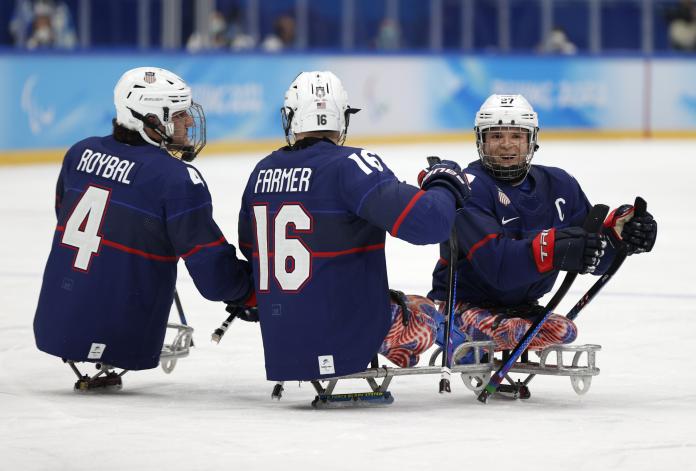 Three players in full Para ice hockey gear celebrating a goal with a smile.