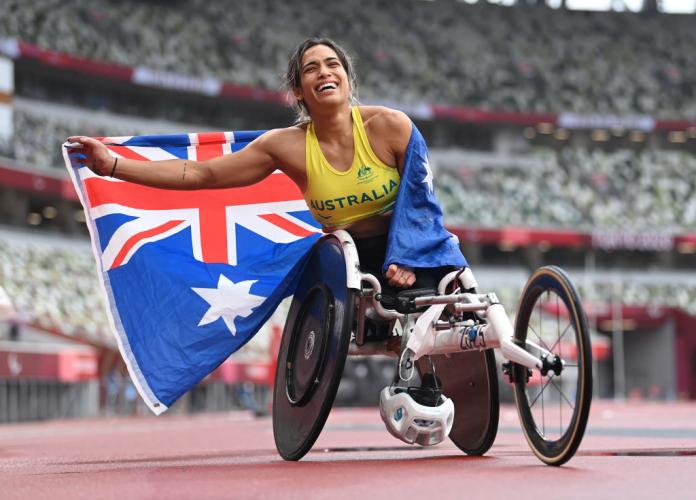 Madison de Rozario celebrates with her national flag on the track at Tokyo 2020 after becoming the first Australian woman to win gold in a Paralympic marathon
