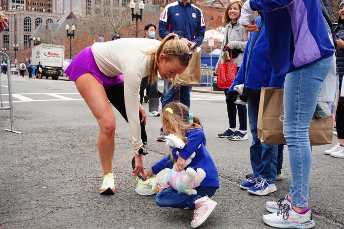 Adrianne Haslet shows her prosthetic left leg to a curious child, who is holding two stuffed toys, as she stops among pedestrians during a training run.