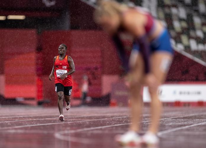 Taonere Banda runs in the women's 400m T13 on a rainy day at Tokyo 2020 while another runner takes a breather at the finish line.