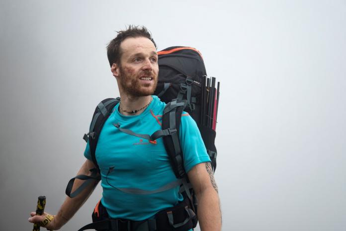 Andrea Lanfri looks into the distance through a heavy fog as he hikes with a large backpack.