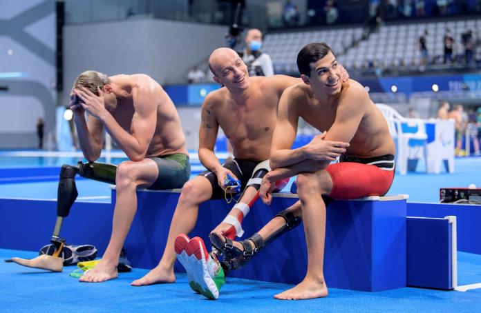 Three male swimmers relax poolside after a race.