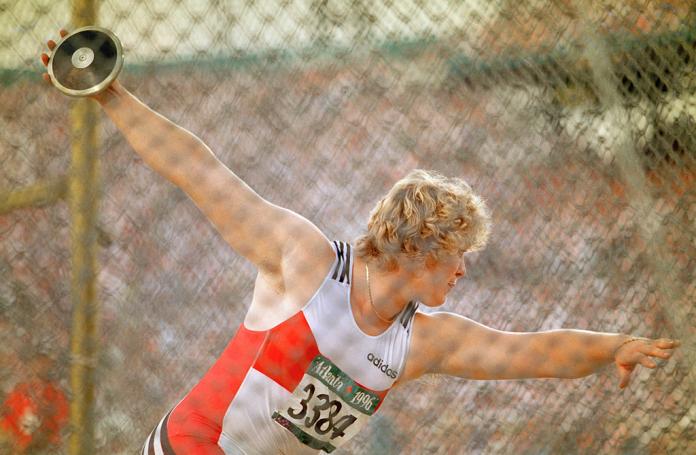 A discus thrower prepares to make a throw, her arms outstretched.
