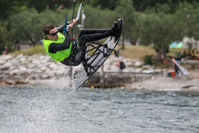 A sitting male kiteboarder rises up from the water creating a splash.