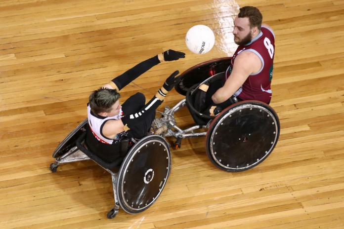Robyn Lambird makes a pass away from a male opponent in a wheelchair rugby match.