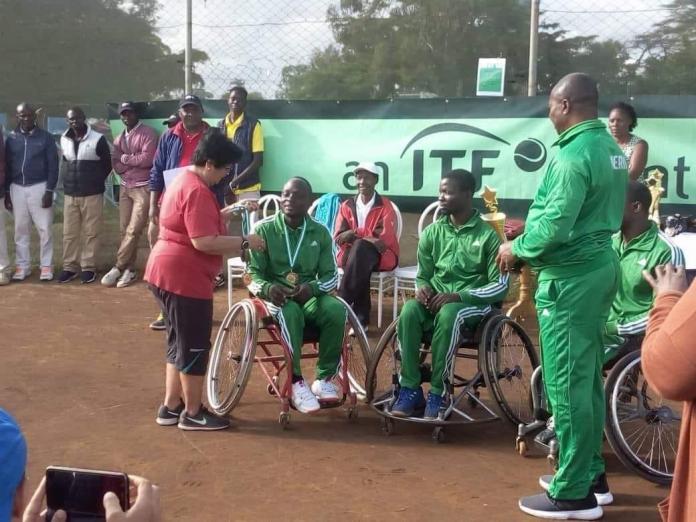 A wheelchair basketball player receives his medal as a group of players and tournament staff look on.