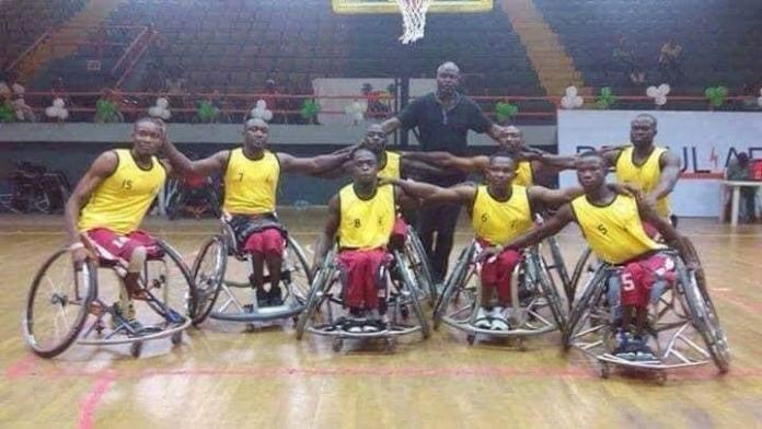 A wheelchair basketball team in yellow jerseys embrace as they take a group photo.