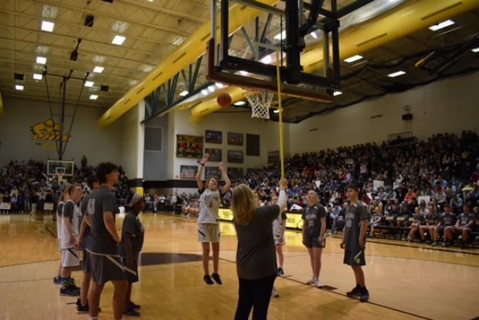 A blind girl in basketball uniform makes a free throw in front of packed stands.