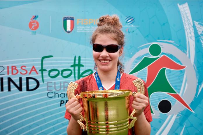 A young athlete holds up a large golden trophy with both hands.