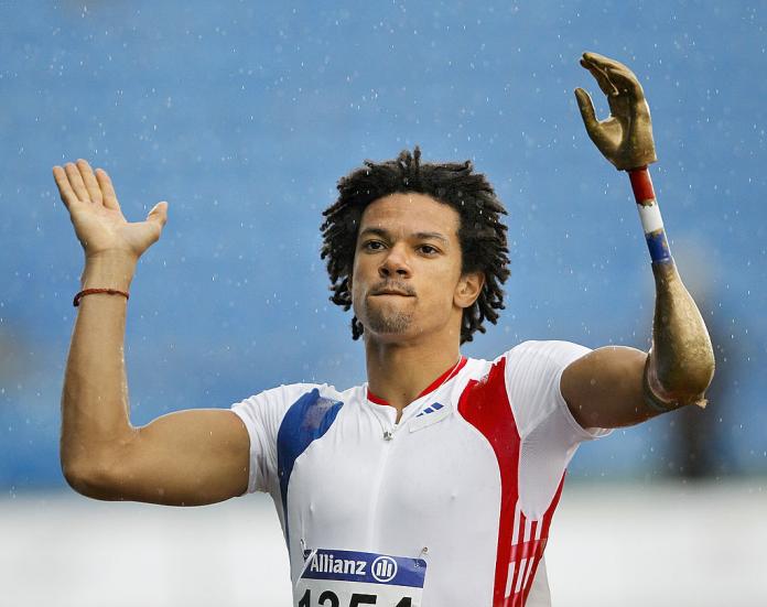 An athlete in French uniform claps as light rain is coming down.