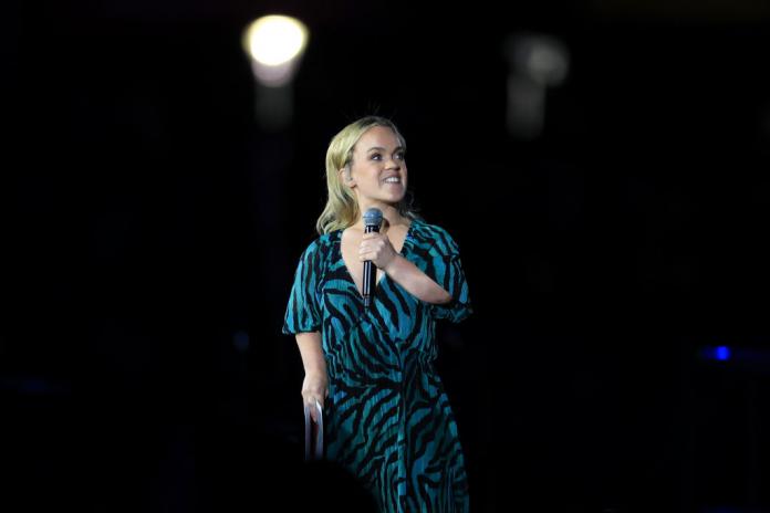 A female athlete in an animal print dress holds a microphone in between the sentences of her speech.