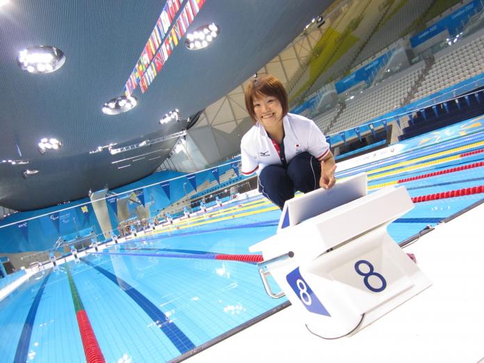 A female athlete poses for a photograph by the pool.