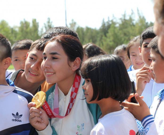 An athlete holds up her gold medal as she poses with children for a photograph.