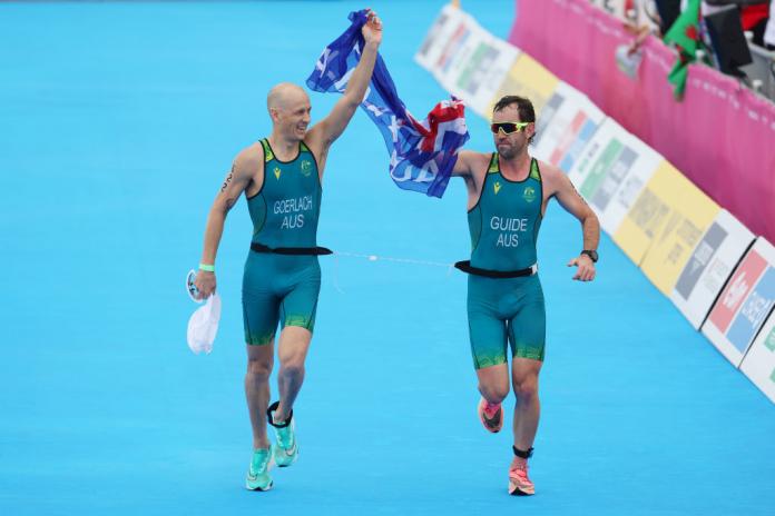 Para triathlete and his guide hold the Australian flag before crossing the finish line at the Commonwealth Games.
