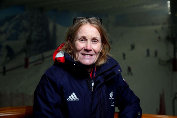 A woman in British uniform poses for a photo in front of a dark ski slope.