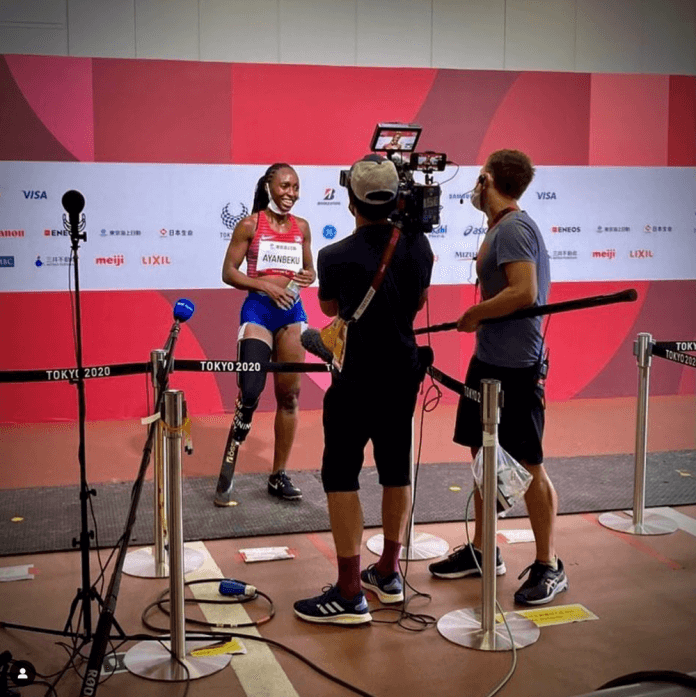 A female sprinter talks to two men carrying filming equipment at the Tokyo 2020 Paralympic Games.