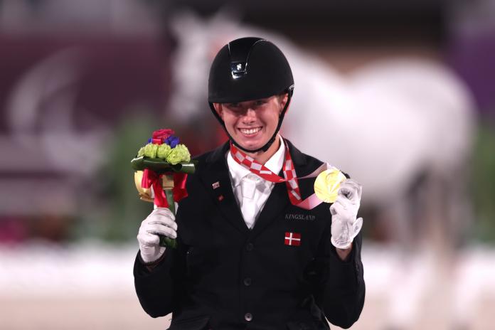 A male athlete smiles as he holds a Tokyo 2020 gold medal with his left hand and a flower bouquet with his right.