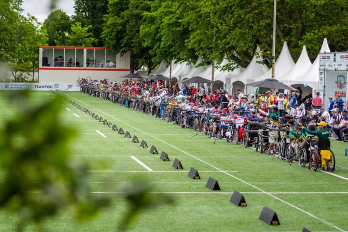Archers in wheelchairs line up to shoot on a green field.