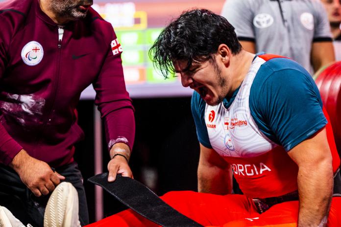 A male powerlifter shouts as he is strapped onto the bench.