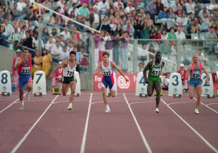 Five men, each missing part of their arm, run down the track in front of a full stadium.