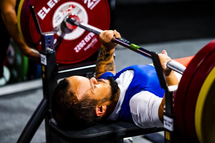 A male powerlifter of short stature prepares to lift a barbell with weights.