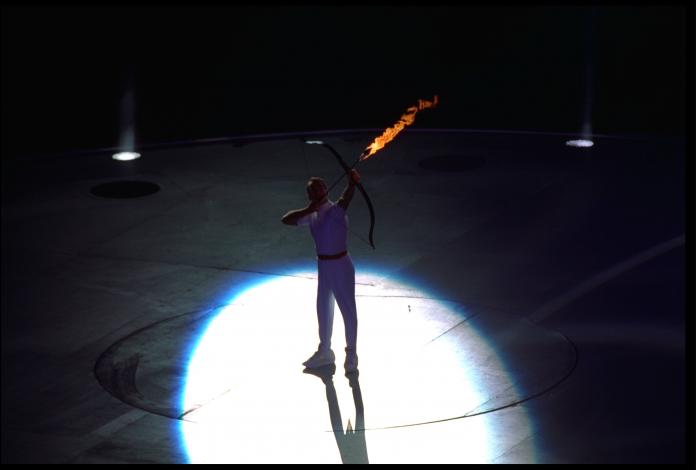 An archer in the spotlight shoots a flaming arrow.