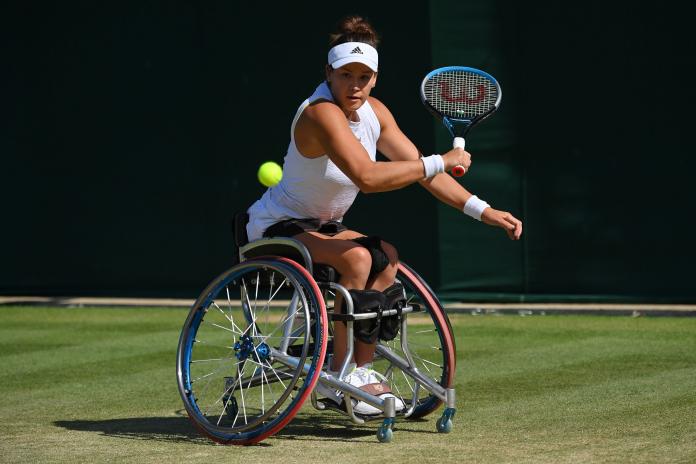 A female wheelchair tennis athlete plays a backhand on a grass court.