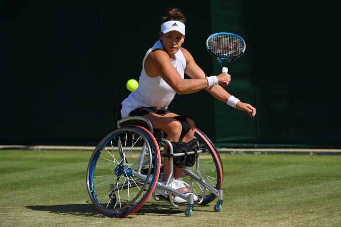 Una atleta de tenis en silla de ruedas juega un revés en una cancha de césped.