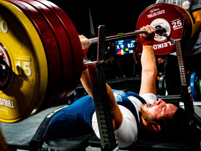 A male powerlifter screams while lifting a barbell with weights.