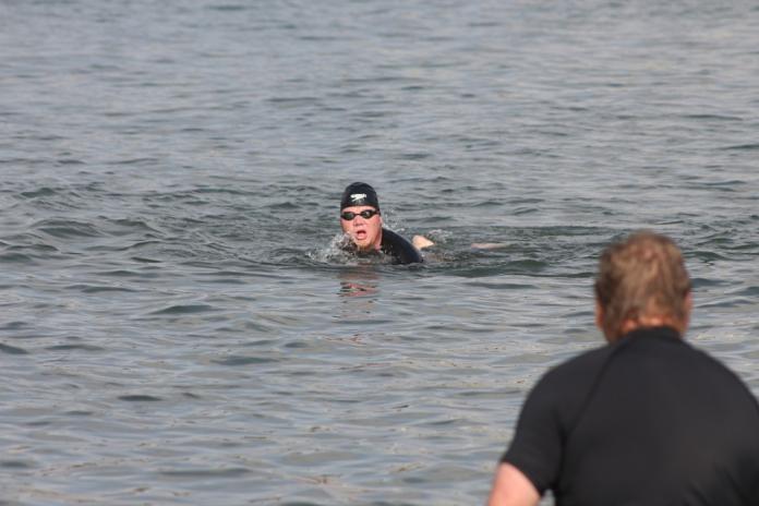 A man swims in open water as another man looks on.