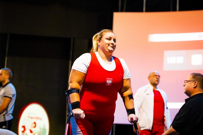 A female powerlifter walks from the competition field with the aid of crutches.