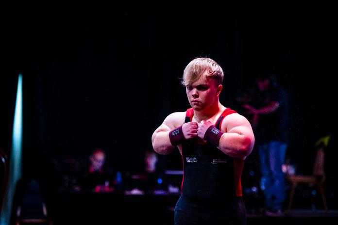 A powerlifter of short stature bumps his fists together as he heads to the bench.