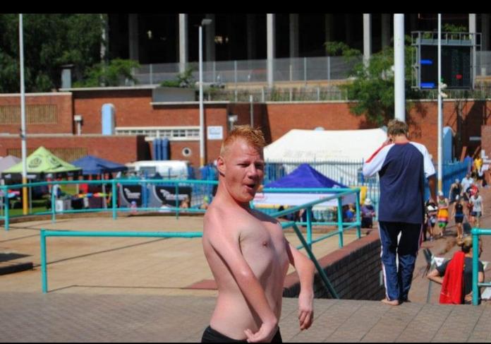 A shirtless swimmer poses for a photo by the pool.