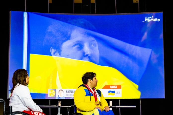 A gold medallist and silver medallist at the victory ceremony while the Ukrainian flag appears on the screen.