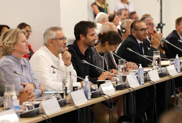 Officials sit in a line at a discussion table equipped with microphone speakers.