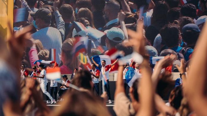 Athletes raise and wave French flags on stage as audience members clap.