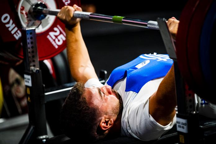 A male powerlifter presses the barbell with a look of effort on his face.