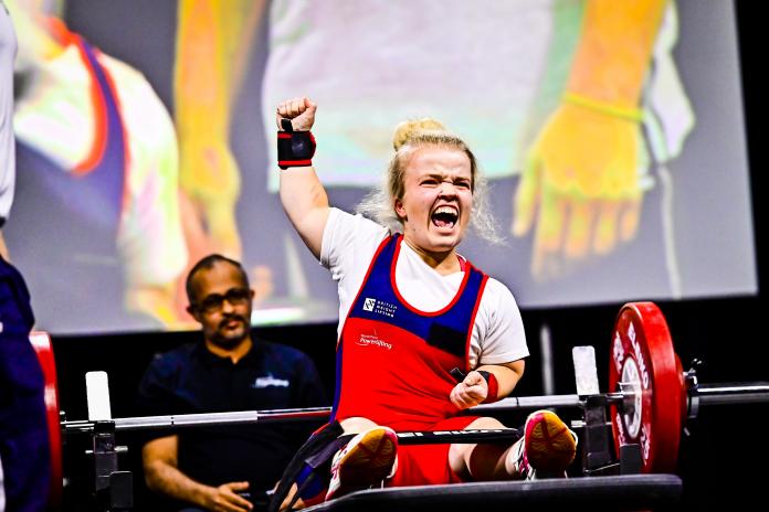 A female Para powerlifter raises her hand in celebration while sitting on the bench.
