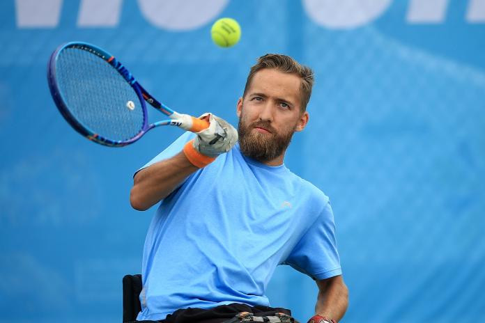 A wheelchair tennis athlete plays a forehand against a blue backdrop.