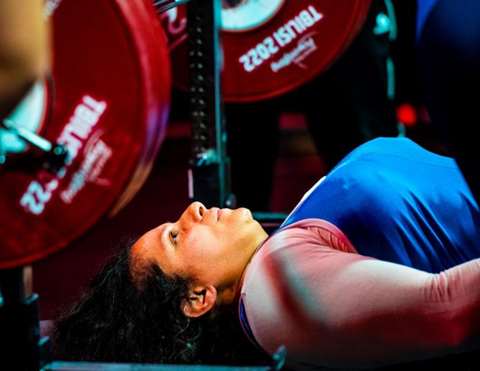 A female powerlifter lies on the bench and looks up at the bar.