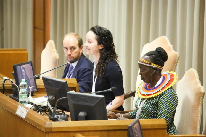 A female athlete, who sits between a two people, makes a speech at an international conference.