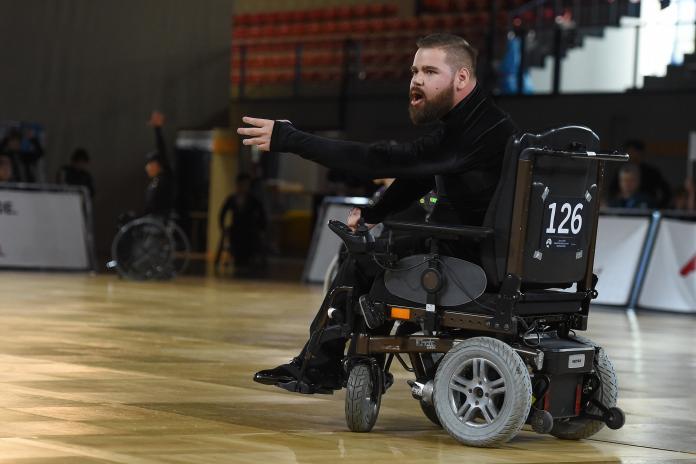 A male Para dancer in an electric wheelchair throws his hand out in a gesture during a dance routine.