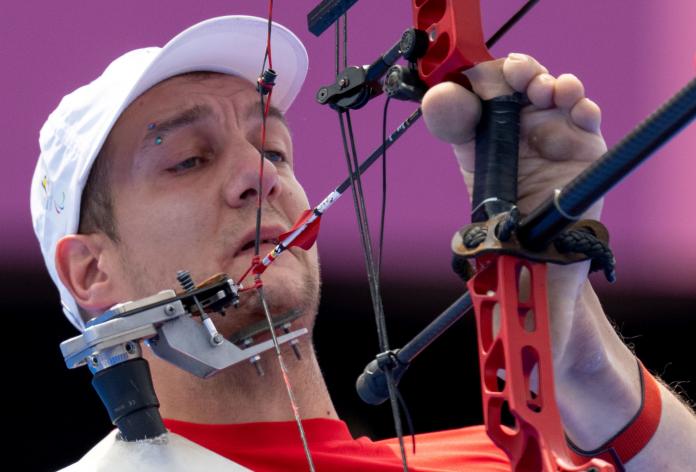 A closeup of a male Para archer who uses his foot to hold the bow.
